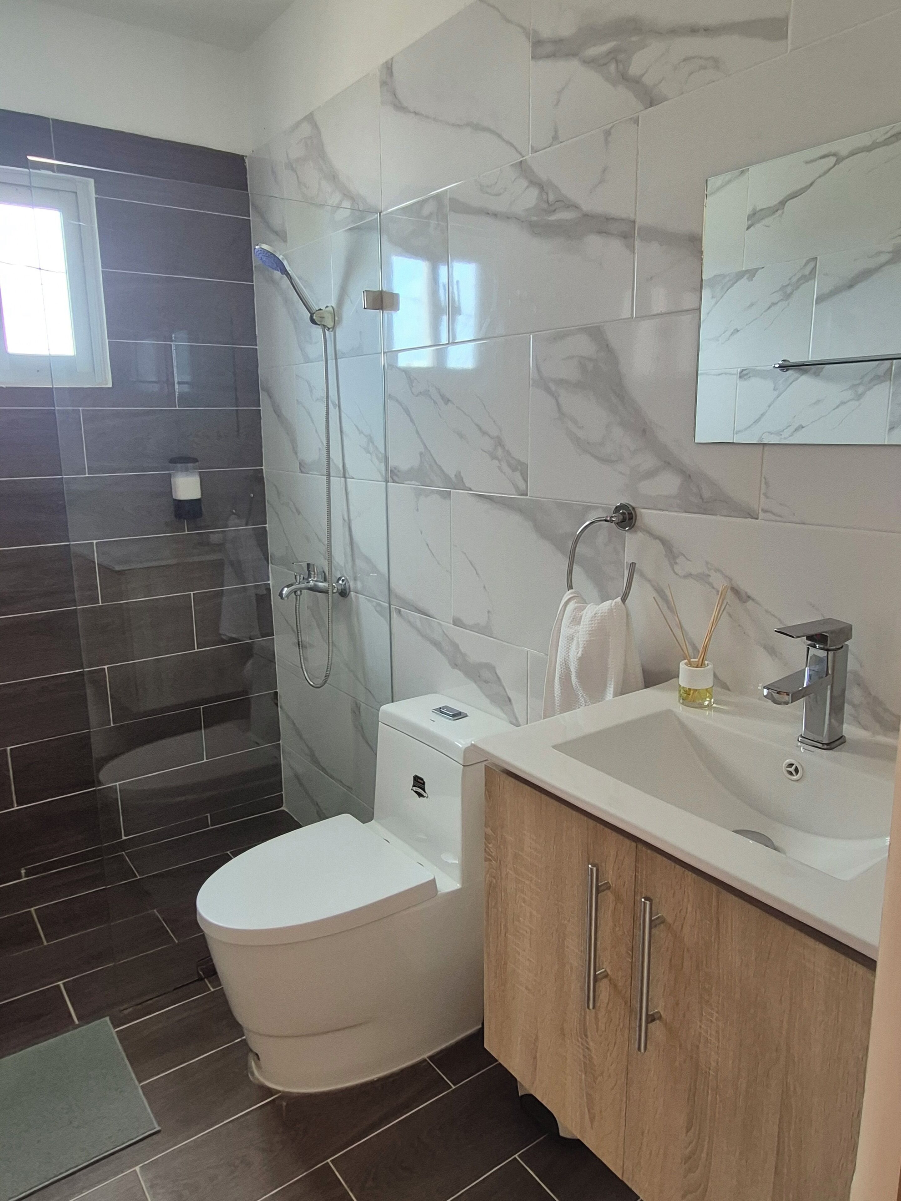 A bathroom with a shower, toilet, sink, and mirror.
