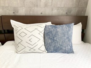 A bed with two pillows, one with a geometric pattern and the other with a textured fabric. - Neo Universal 02 (Osaka, Konohana Ward, Nishikujo)