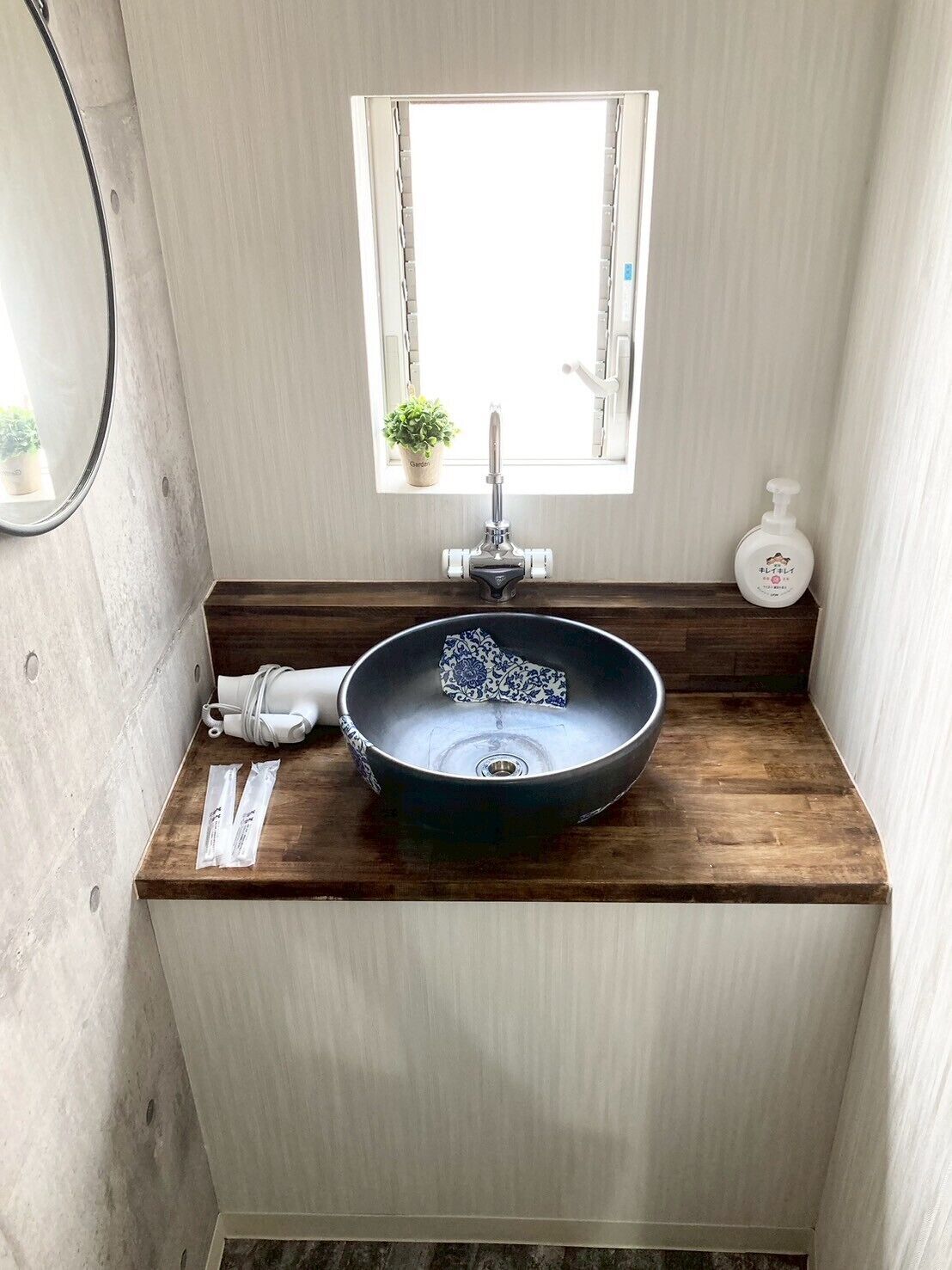 A bathroom with a wooden countertop, a black sink with a faucet, a small window with a plant, and a soap dispenser.