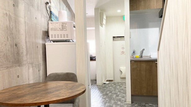 A room with a round wooden table and a grey chair, a white cabinet with a paper towel dispenser, and a tiled floor. - Neo Universal 02 (Osaka, Konohana Ward, Nishikujo)