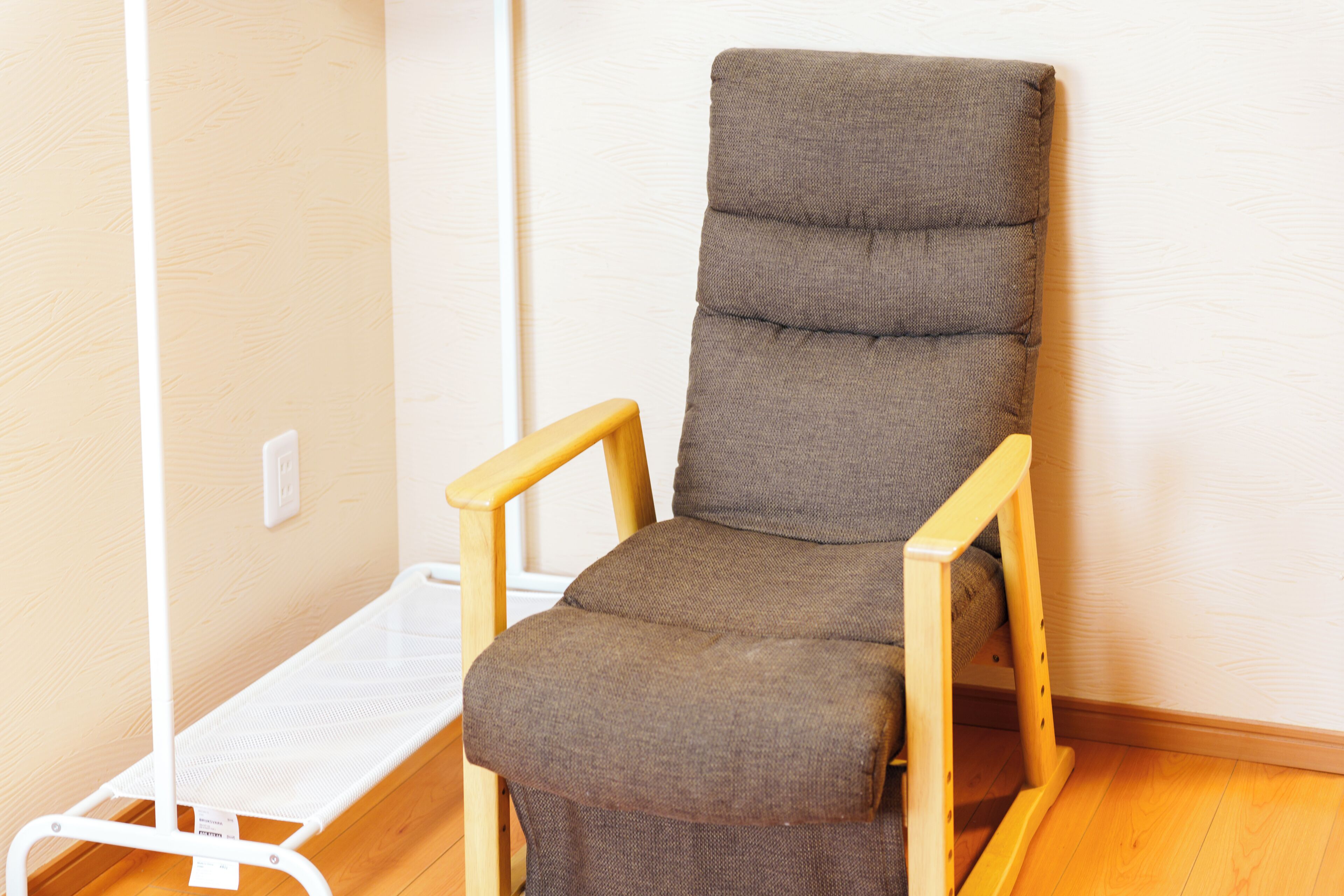 A wooden chair with a cushioned seat and backrest, positioned against a wall with a white baseboard and a wooden floor.