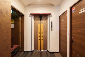 An elevator with a yellow stripe and black squares, flanked by wooden doors with a sign above. - SERENE | Dotonbori · 5th Floor | 80 ㎡ · 3 bedrooms · 2 bathrooms | Japanese-style room | Entire Floor (Osaka)