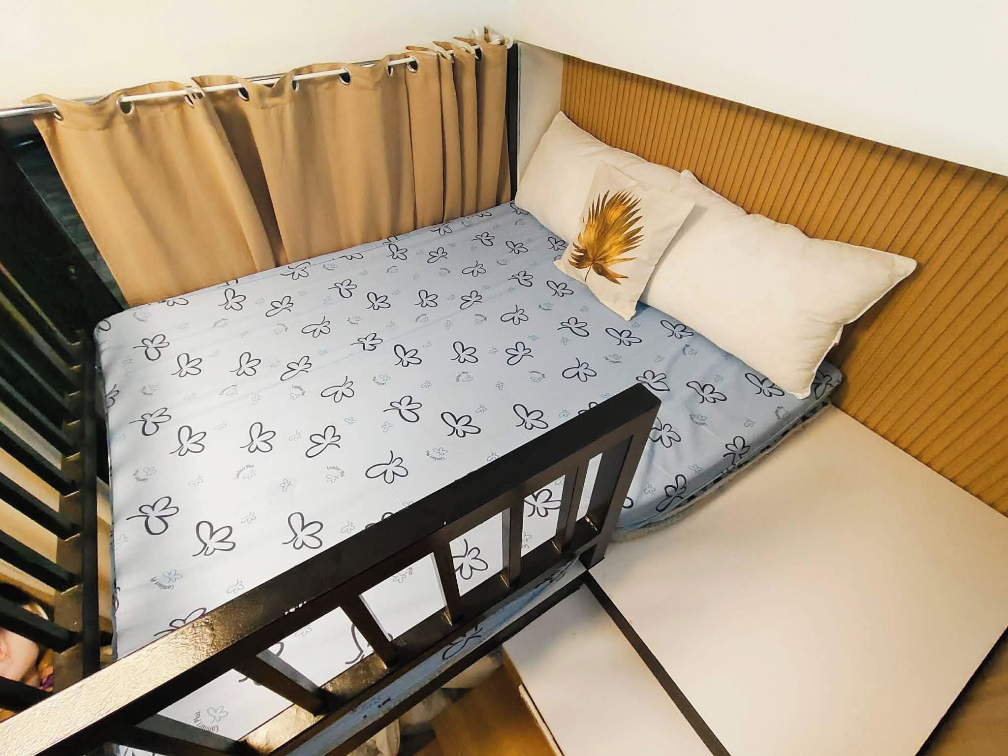 A small bed with a patterned bedspread, a pillow with a feather design, and a wooden headboard.