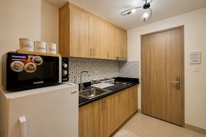 A compact kitchen with wooden cabinets, a microwave oven, and a sink. - Luxury Pool View Condo Near MOA | Smart Lock | Netflix (Pasay City)