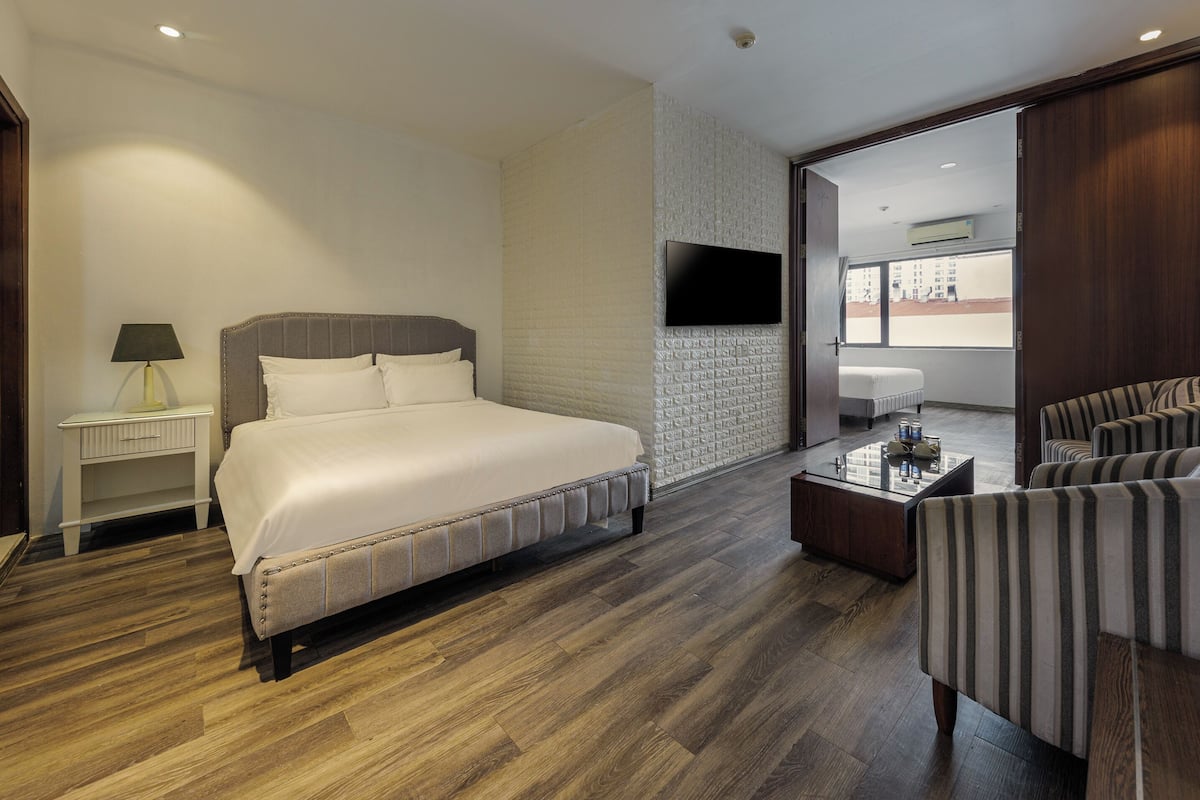 Une chambre d’hôtel avec un grand lit, un téléviseur fixé au mur, un coin salon avec des chaises à rayures et un plancher en bois.