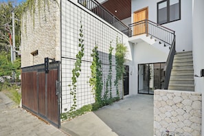 A modern building with a stone facade, a wooden gate, and a staircase leading to a balcony. - Azure Villa by Kozystay - Jimbaran (Badung)