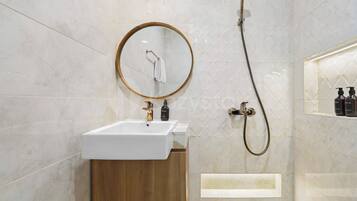 Ein modernes Badezimmer mit einem weißen Waschbecken, einem runden Spiegel, einer Handbrause und einem Holzkabinett.