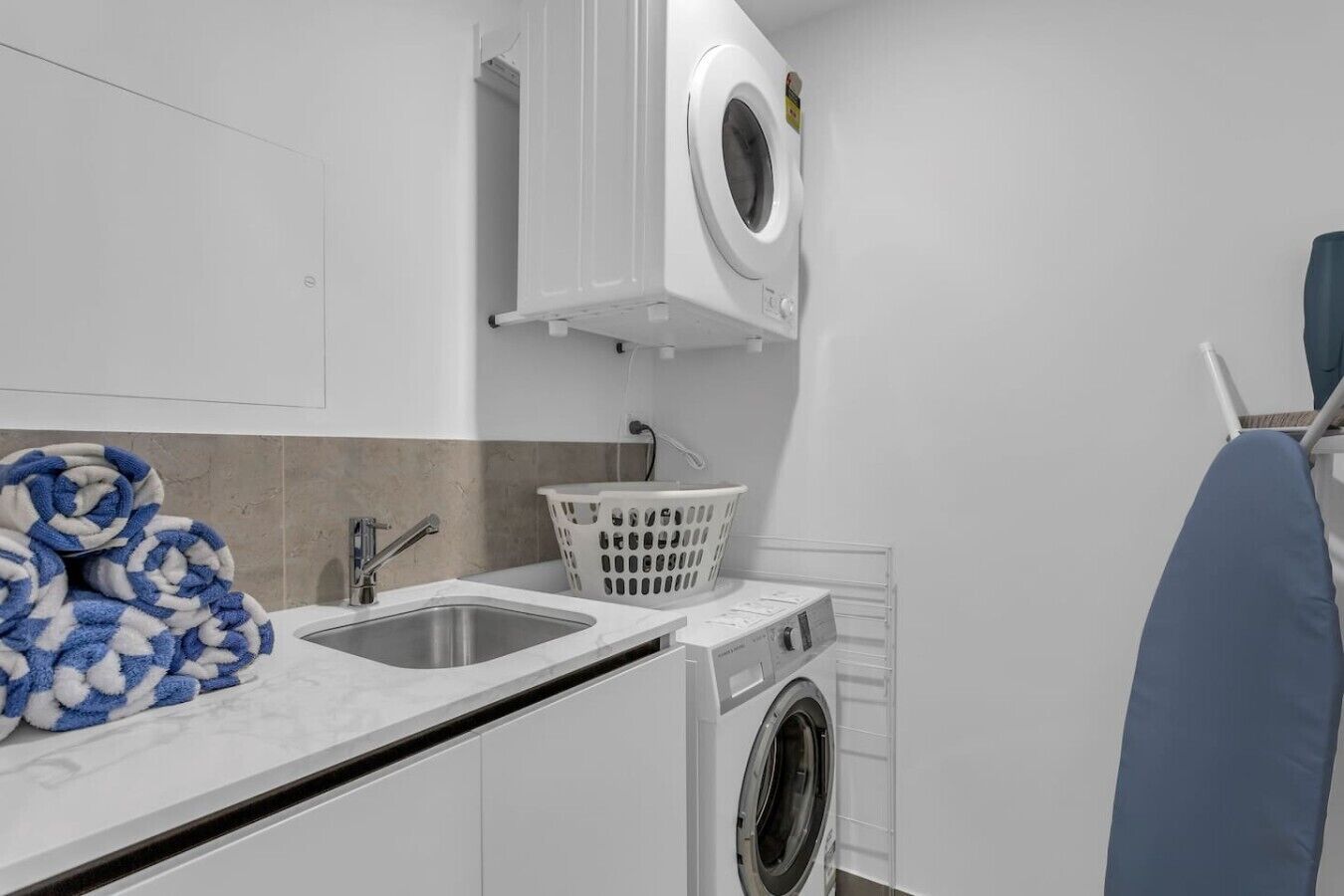 Une petite buanderie équipée d’un lave-linge, d’un évier et d’un étendoir.
