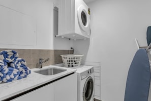 A compact laundry room with a washing machine, a sink, and a drying rack. - Luxury 14th Floor 3 Brm Apt with Beach Views (Broadbeach)