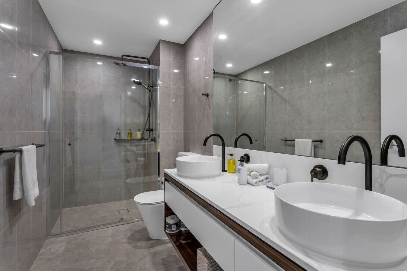 A modern bathroom with a glass-enclosed shower, two sinks, and a large mirror.