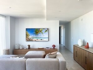Ein modernes Wohnzimmer mit einem großen Flachbildfernseher an der Wand, einer Holzkommode und einem Sofa mit Kissen.