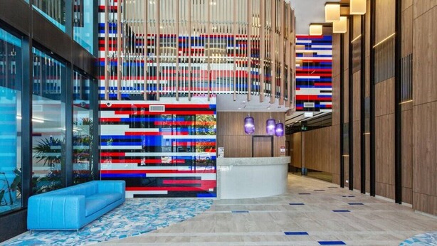 A modern lobby with a reception desk, seating area, and a decorative wall with vertical elements. - Lvl 15 Luxury 2 Bedroom APT with Beach Views (Broadbeach)