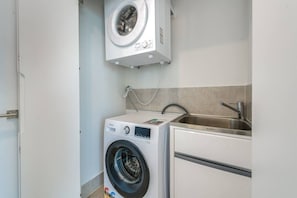 A compact laundry room with a front-loading washer and dryer, a stainless steel sink, and a tiled backsplash. - Luxury L16  2 bedroom APT with Beach Views (Broadbeach)