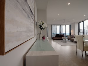 Un salon moderne avec un grand tableau abstrait, une table basse en verre et une vue sur la ville grâce à de grandes fenêtres.