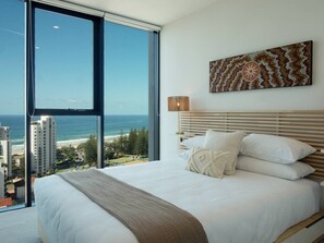 Ein Schlafzimmer mit einem großen Bett, Blick auf den Ozean und die Stadtlandschaft.