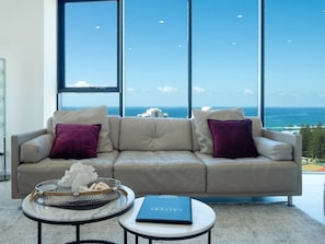 A modern living room with a large window offering a view of the ocean. - L18 Stunning 3 BRM Apt with Beach Views (Broadbeach)