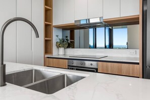 A modern kitchen with a stainless steel sink, a built-in stove, and wooden cabinetry. - Stunning L19 Dlx 3 Bedroom Apt w/ Hinterland Views (Broadbeach)