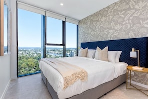 A bedroom with a large bed, a view of a cityscape, and a patterned wall. - Stunning L19 Dlx 3 Bedroom Apt w/ Hinterland Views (Broadbeach)