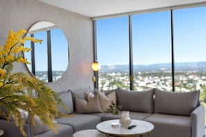 A modern living room with a grey sofa, a round coffee table, and a large window offering a city view. - Stunning L19 Dlx 3 Bedroom Apt w/ Hinterland Views (Broadbeach)