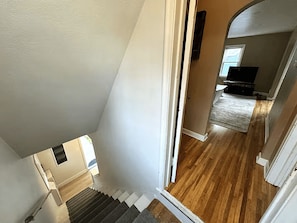 A staircase leading to a living area with a wooden floor and a television in the background. - Kutzky Duplex: Walk to Mayo 2BR with Free Parking (Rochester)