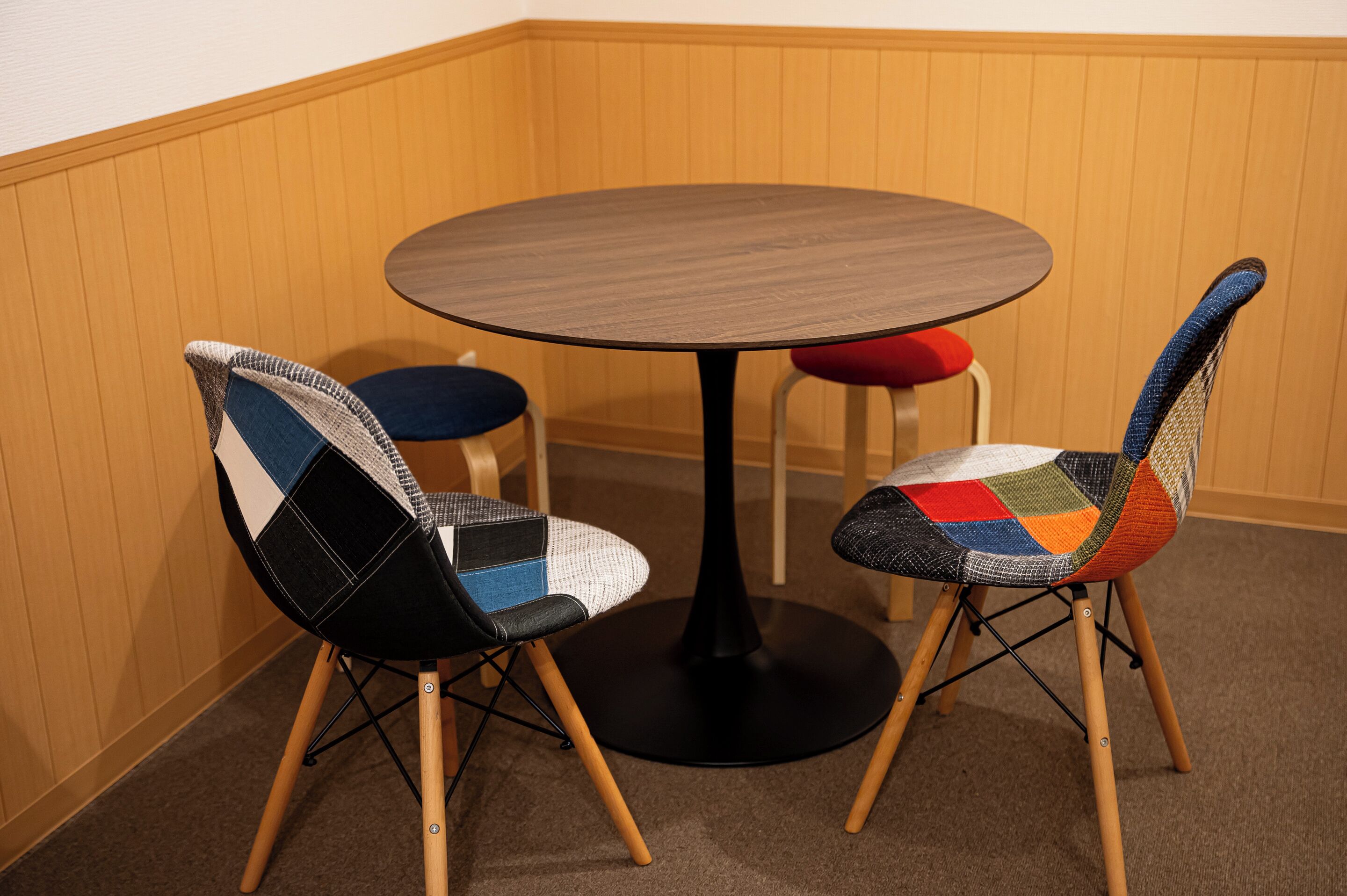 A corner room with a round table and two chairs with colorful fabric upholstery.
