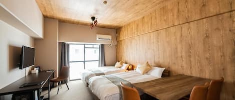 A hotel room with a wooden ceiling, a bed with white linens, a desk with a computer, and a dining table with chairs.