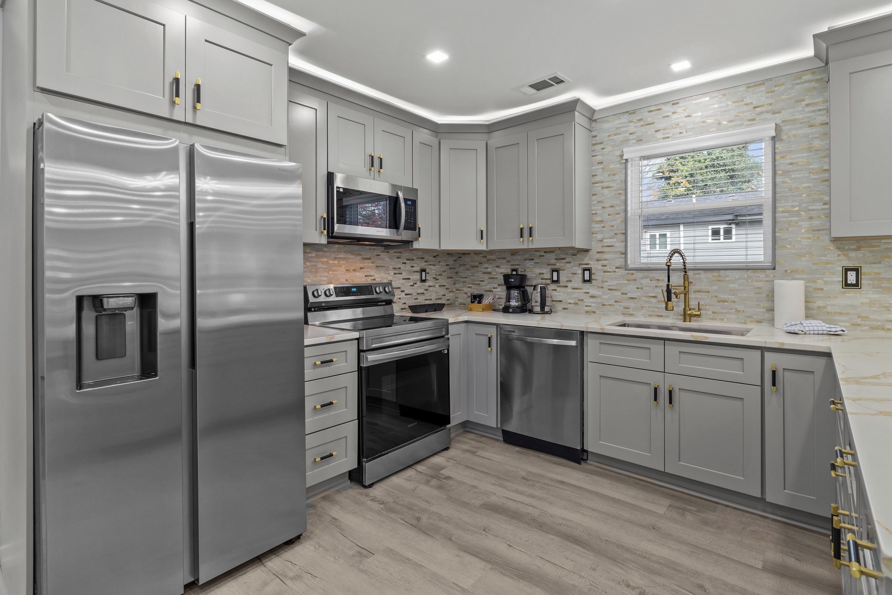 A modern kitchen with stainless steel appliances, grey cabinetry, and a tiled backsplash.