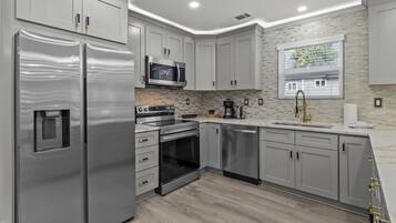 A modern kitchen with stainless steel appliances, grey cabinetry, and a tiled backsplash.