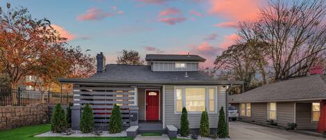 A modern two-story house with a red door, a well-maintained lawn, and a driveway leading to the entrance.