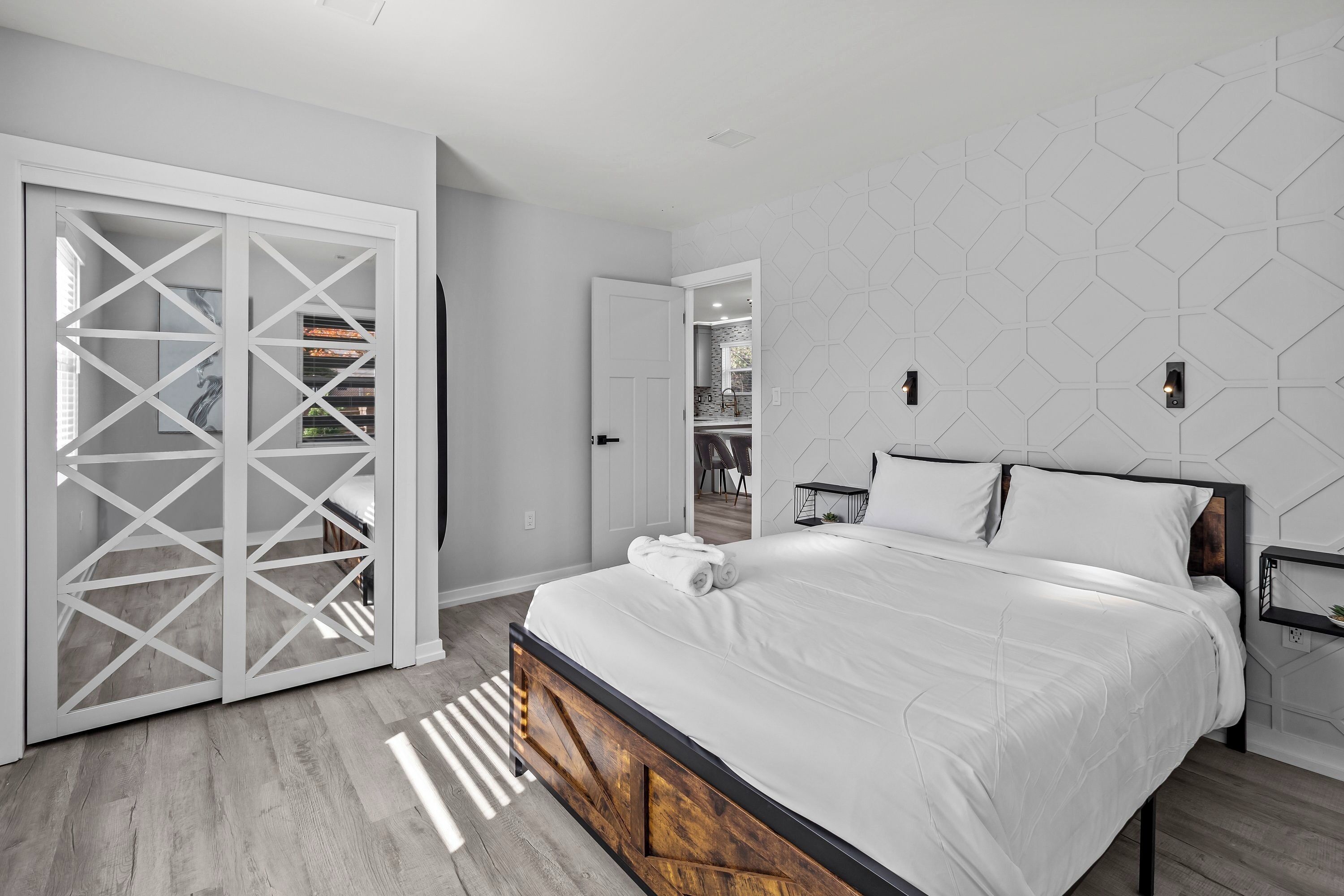 A modern bedroom with a bed, a wardrobe, and a geometric wall design.