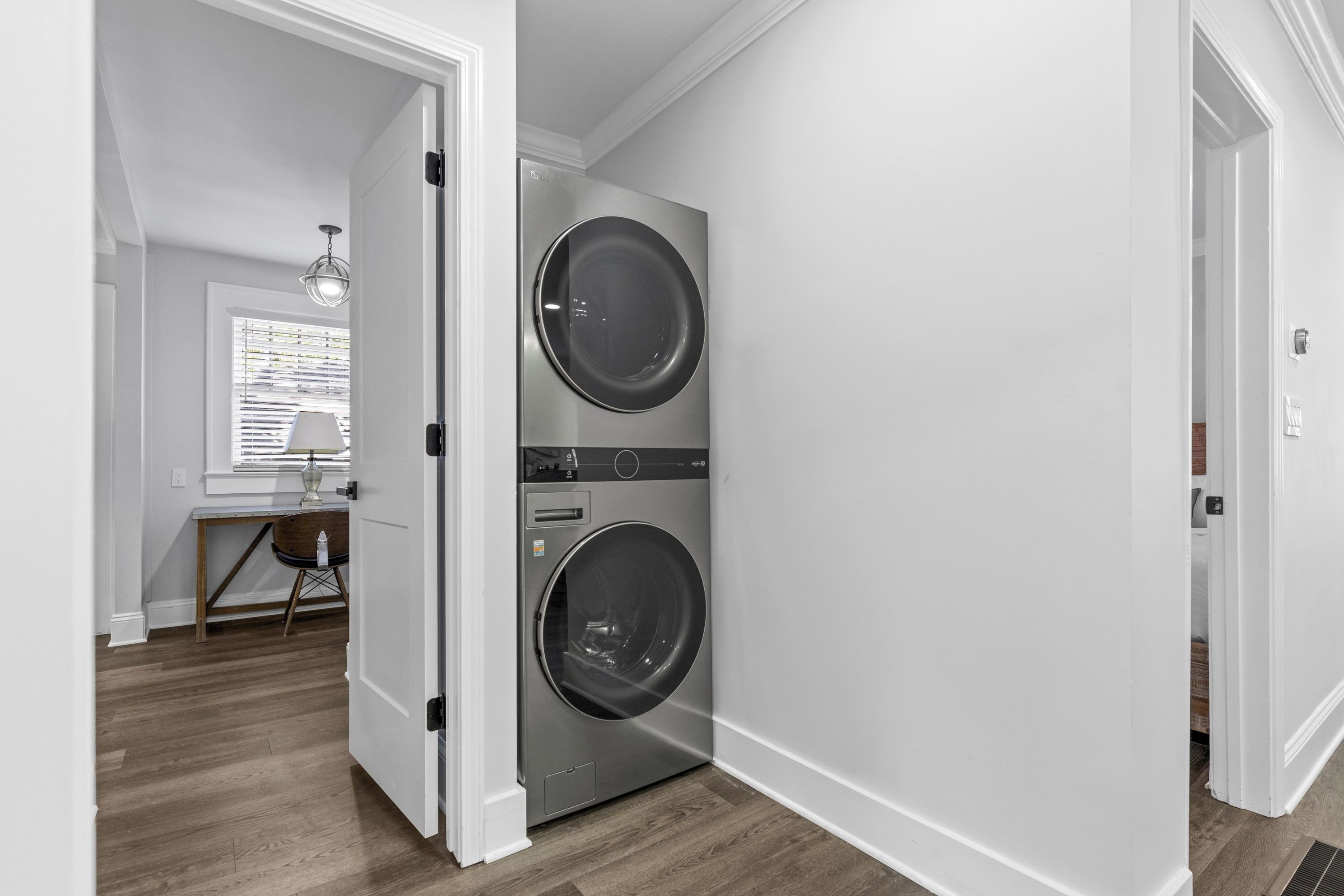 A laundry room with two stacked front-loading washing machines, a wooden floor, and a door leading to another room.