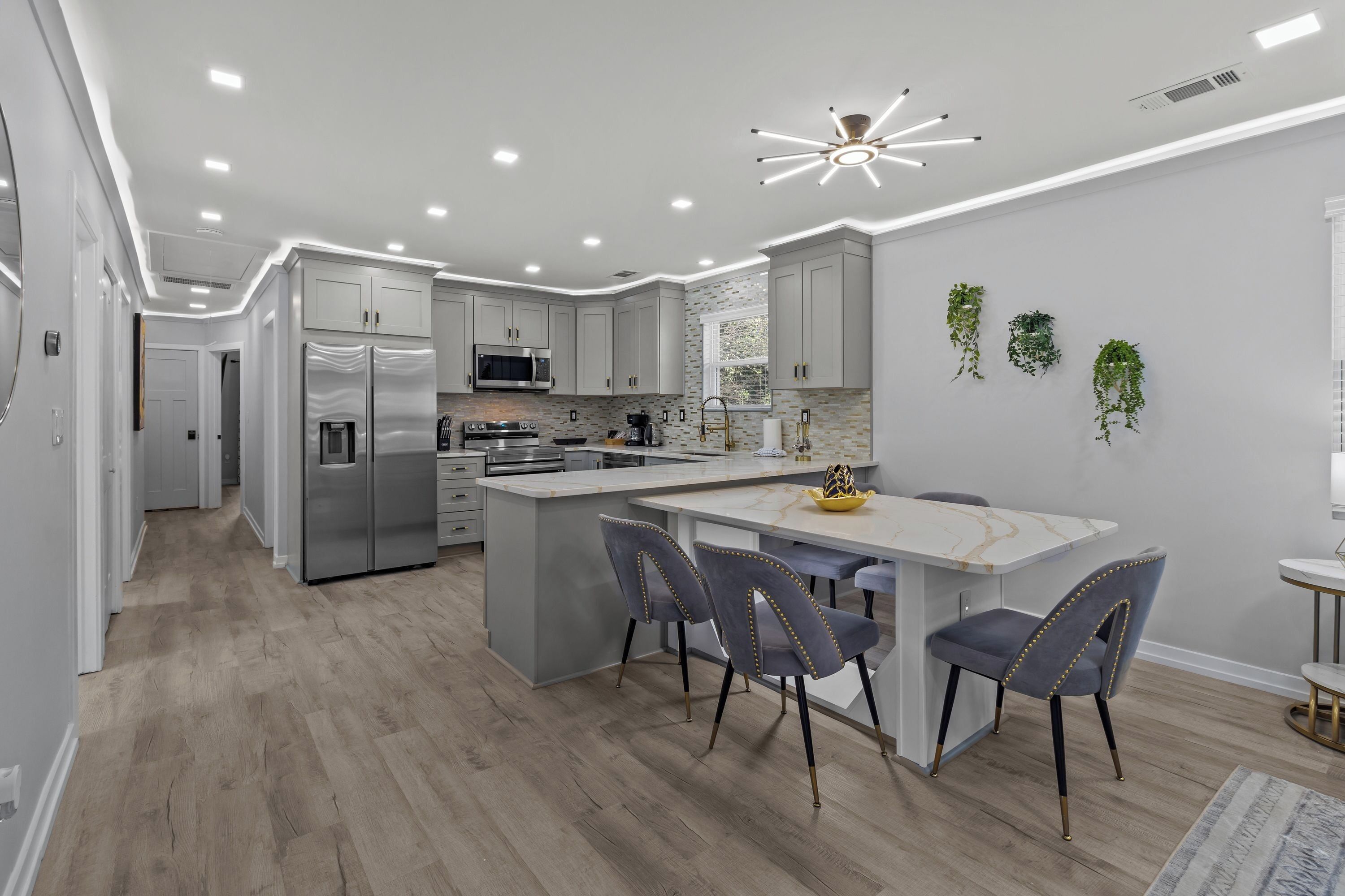 Une cuisine moderne dotée d’un îlot central, d’appareils électroménagers en acier inoxydable et d’un ventilateur de plafond.