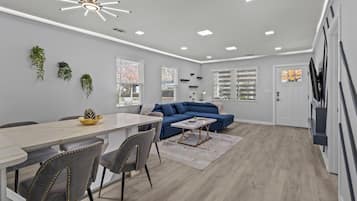 A modern living room with a blue sofa, a dining table with chairs, and a ceiling light fixture.