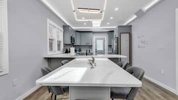 Una cocina moderna con gabinetes grises, una isla de mármol blanco y una lámpara colgante.