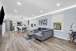 A modern living room with a grey sofa, a dining area, and a kitchen in the background.