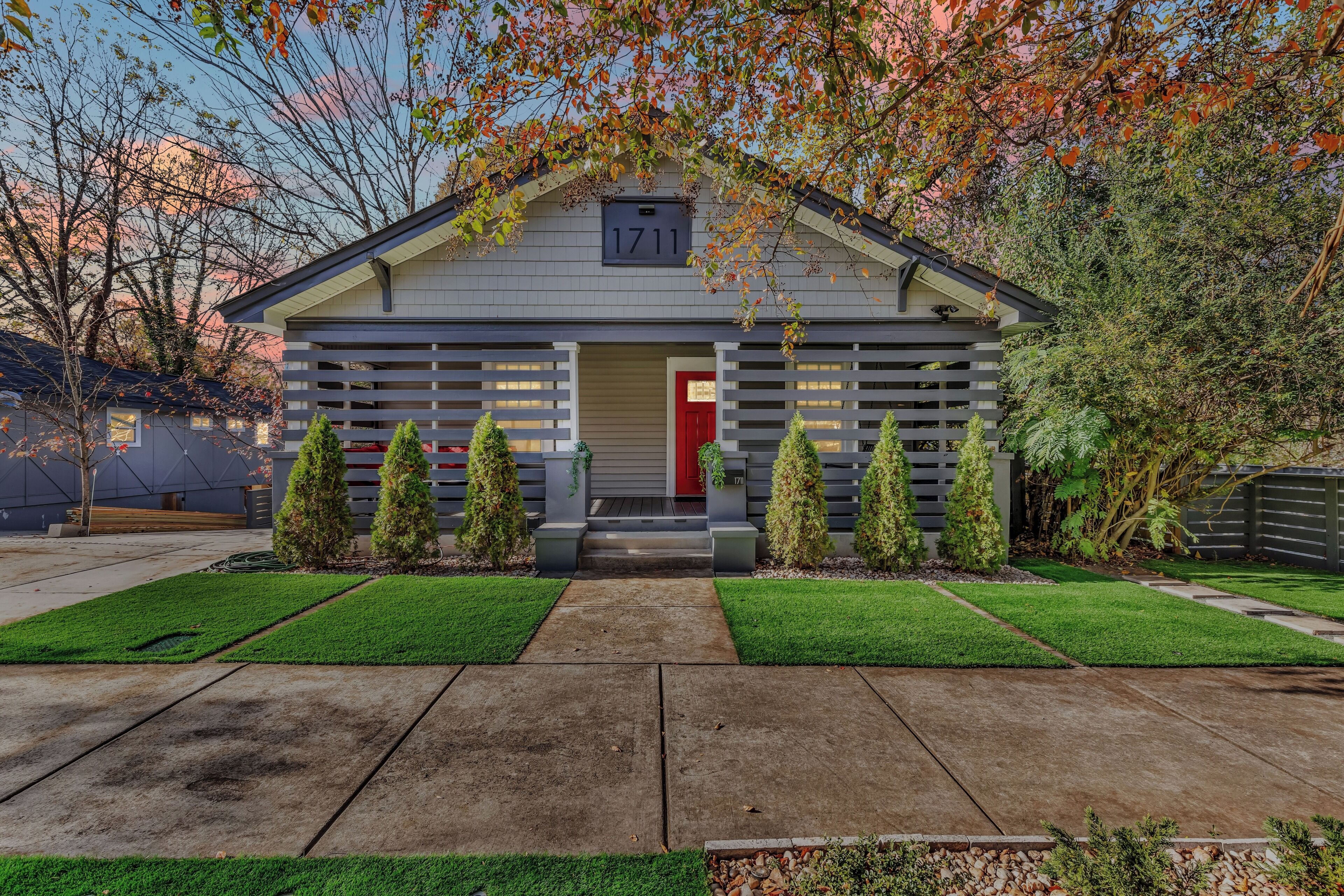 A modern building with a red door, numbered 1711, featuring a symmetrical front with evenly spaced trees and a well-maintained lawn.