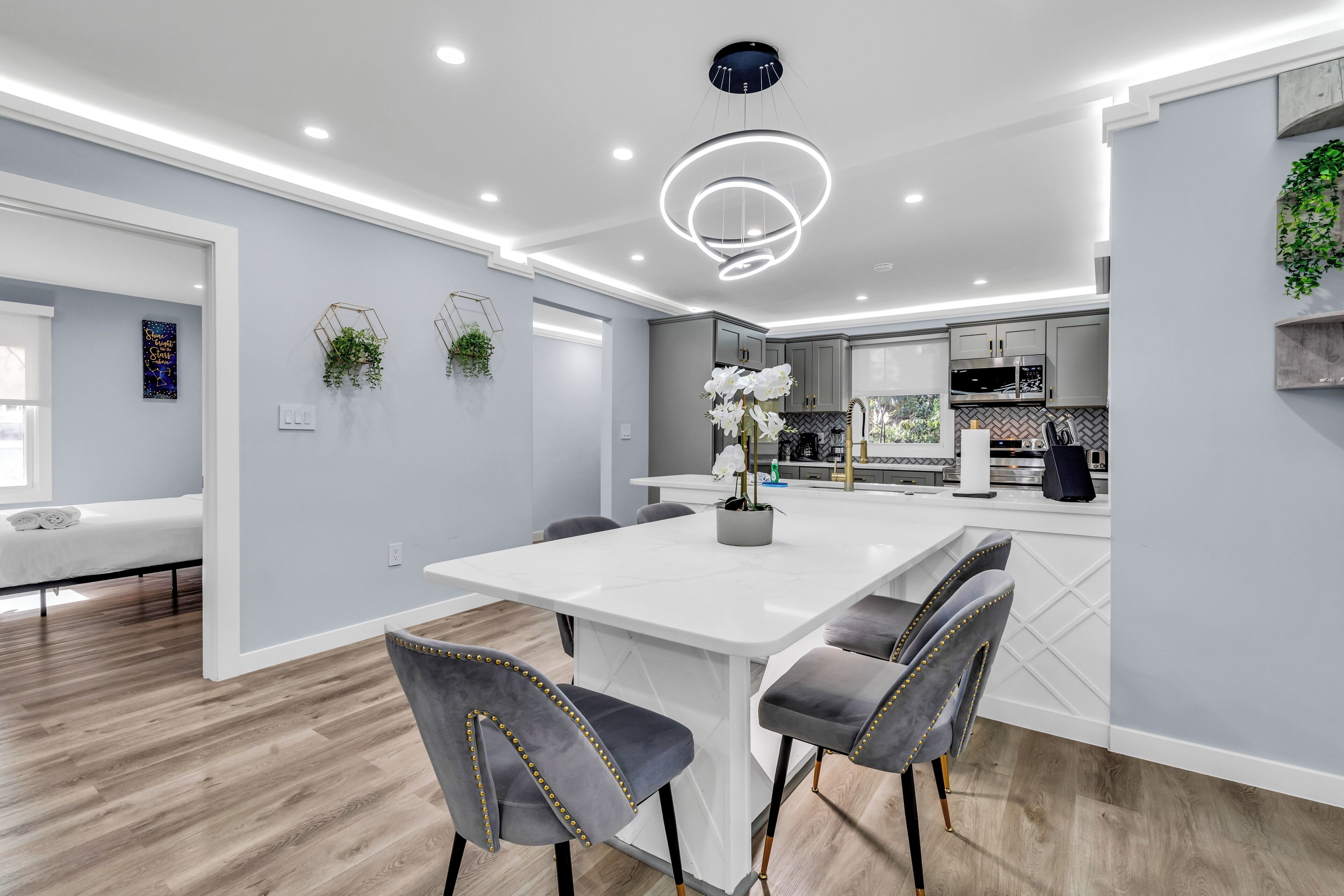 A modern dining area with a white table, grey upholstered chairs, and a central light fixture.