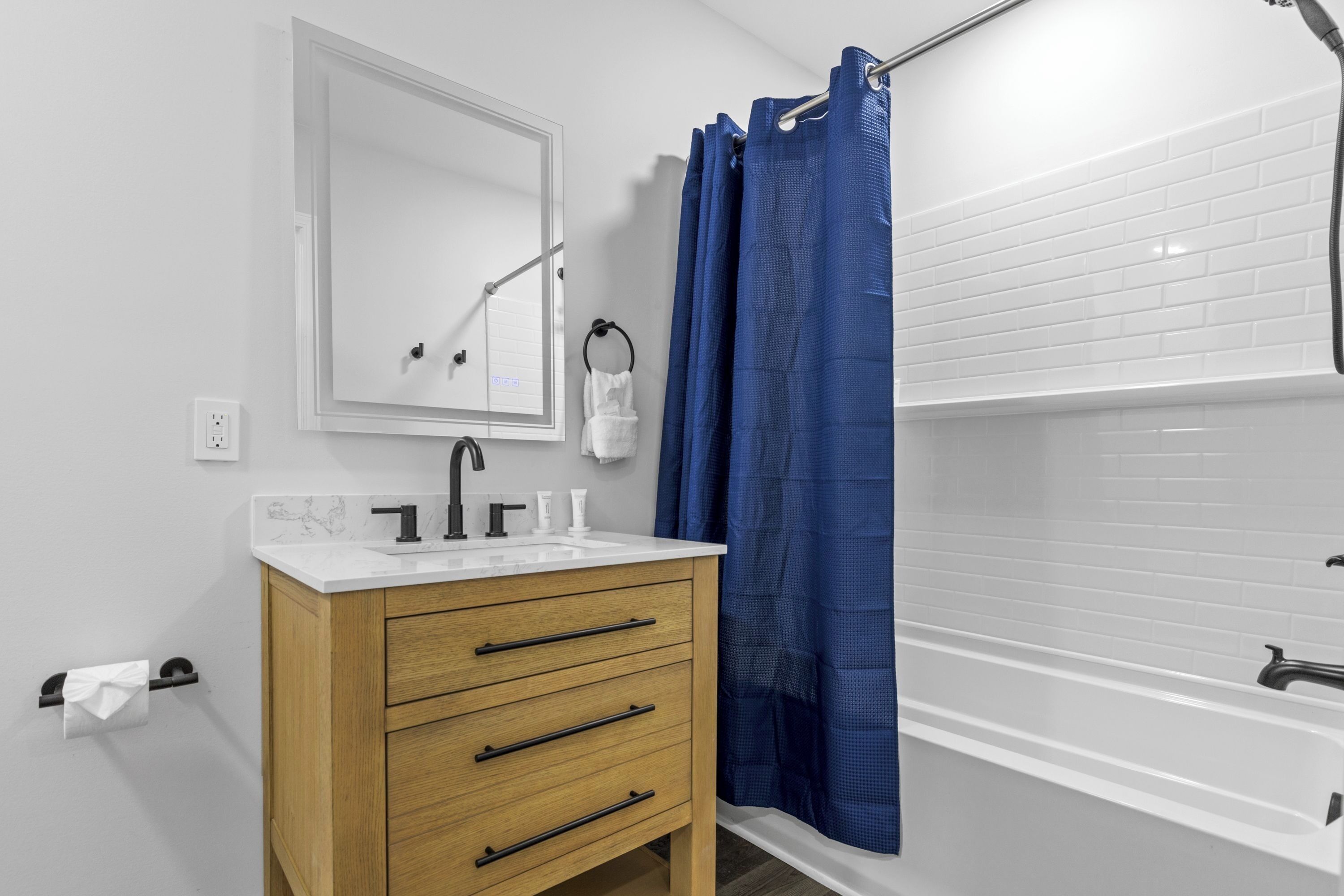 A bathroom with a white sink, wooden vanity, a mirror, a towel rack, and a blue shower curtain.