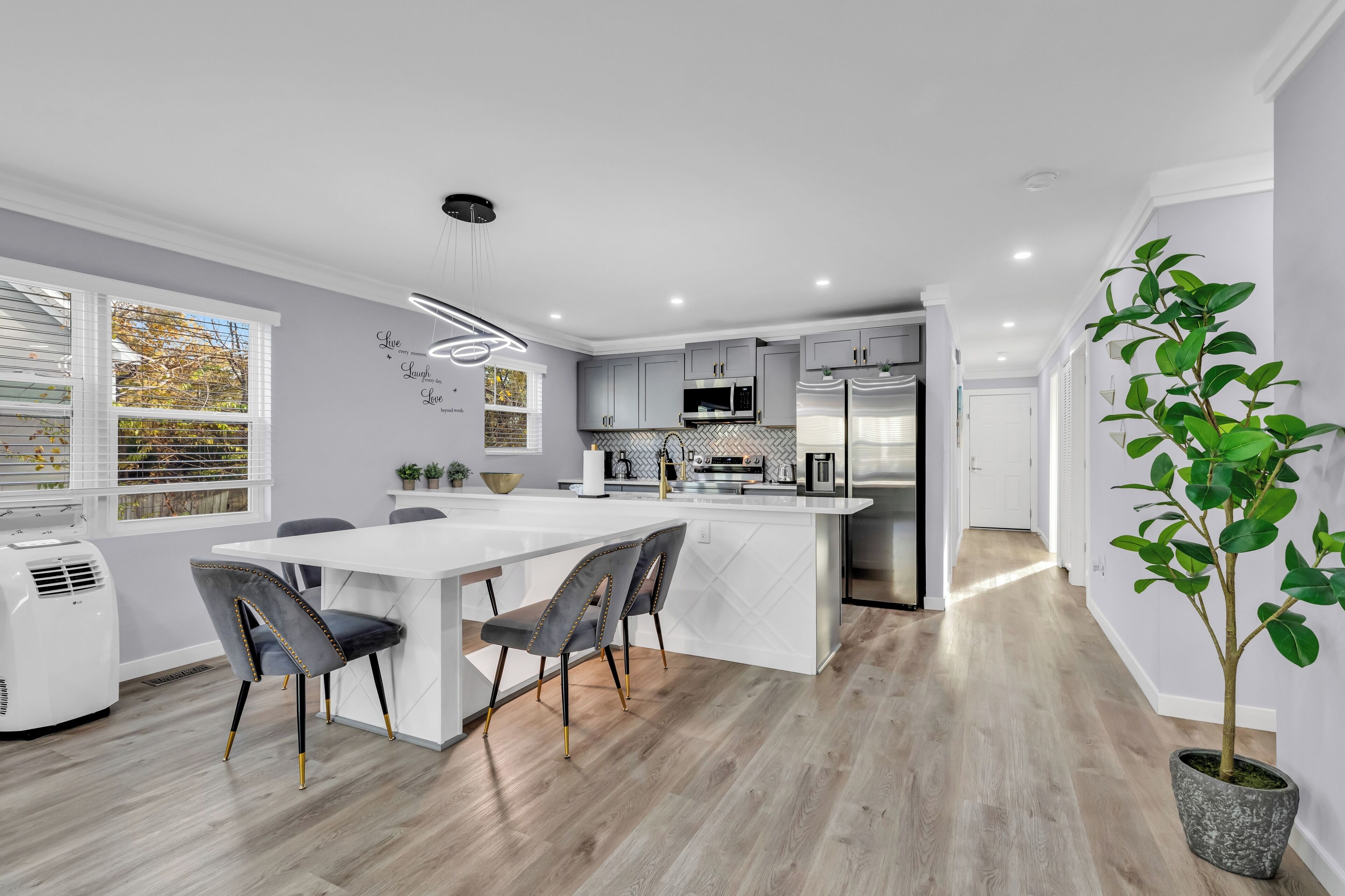 A modern kitchen with a central island, grey cabinetry, and a dining area with a white table and chairs.
