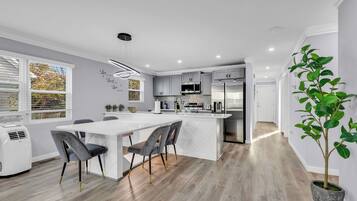 A modern kitchen with a central island, grey cabinetry, and a dining area with a white table and chairs.