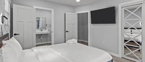 Un dormitorio con una cama grande, un baño con espejo y un televisor montado en la pared.