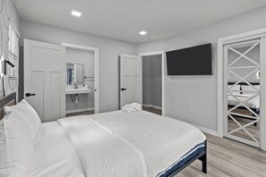 Un dormitorio con una cama grande, un baño con espejo y un televisor montado en la pared.