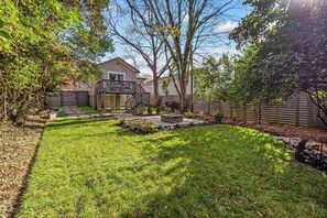Un patio trasero residencial con césped, una terraza de madera y una casa al fondo.