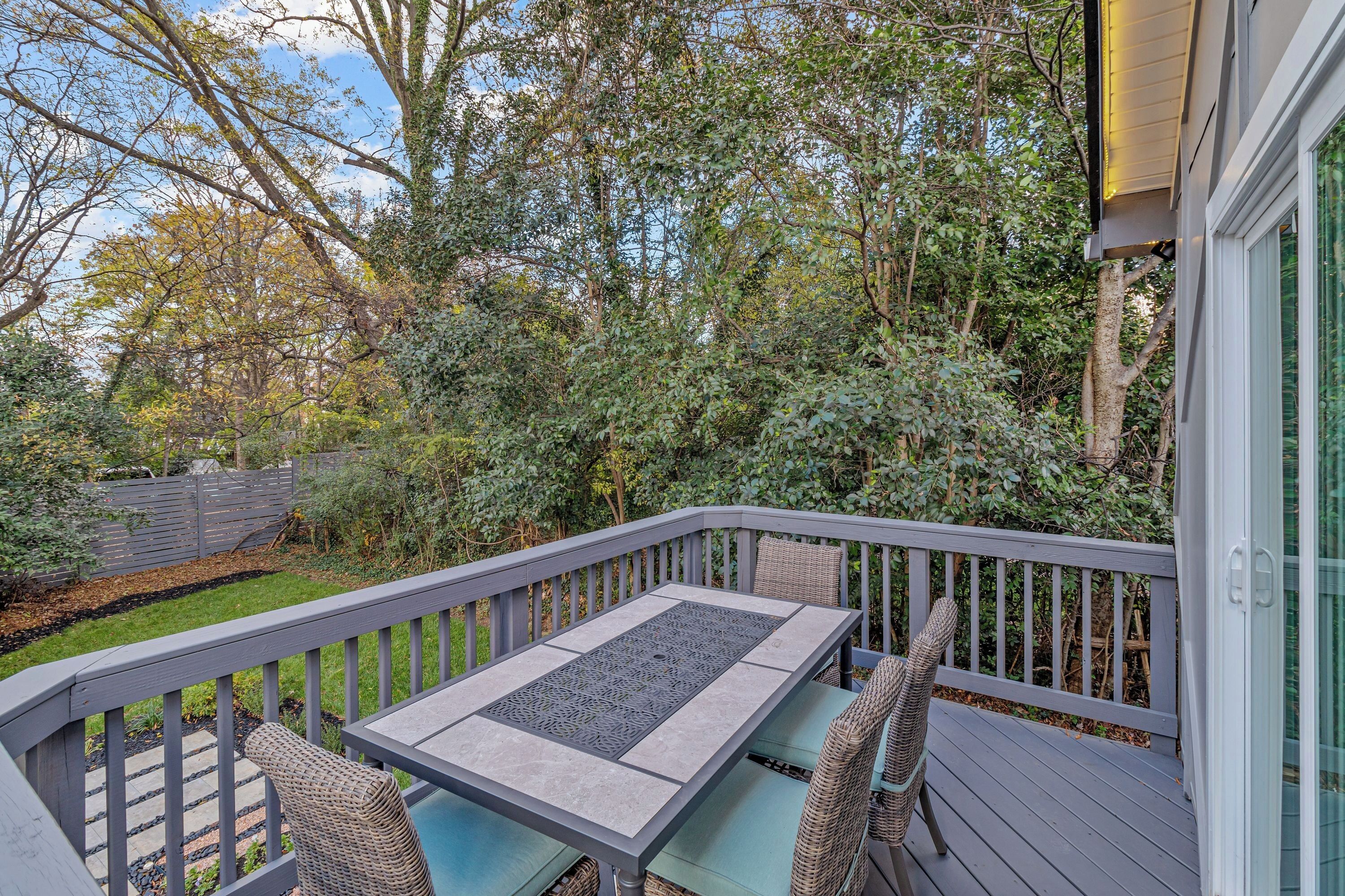 A deck with a table and chairs, surrounded by a wooden fence and dense foliage.