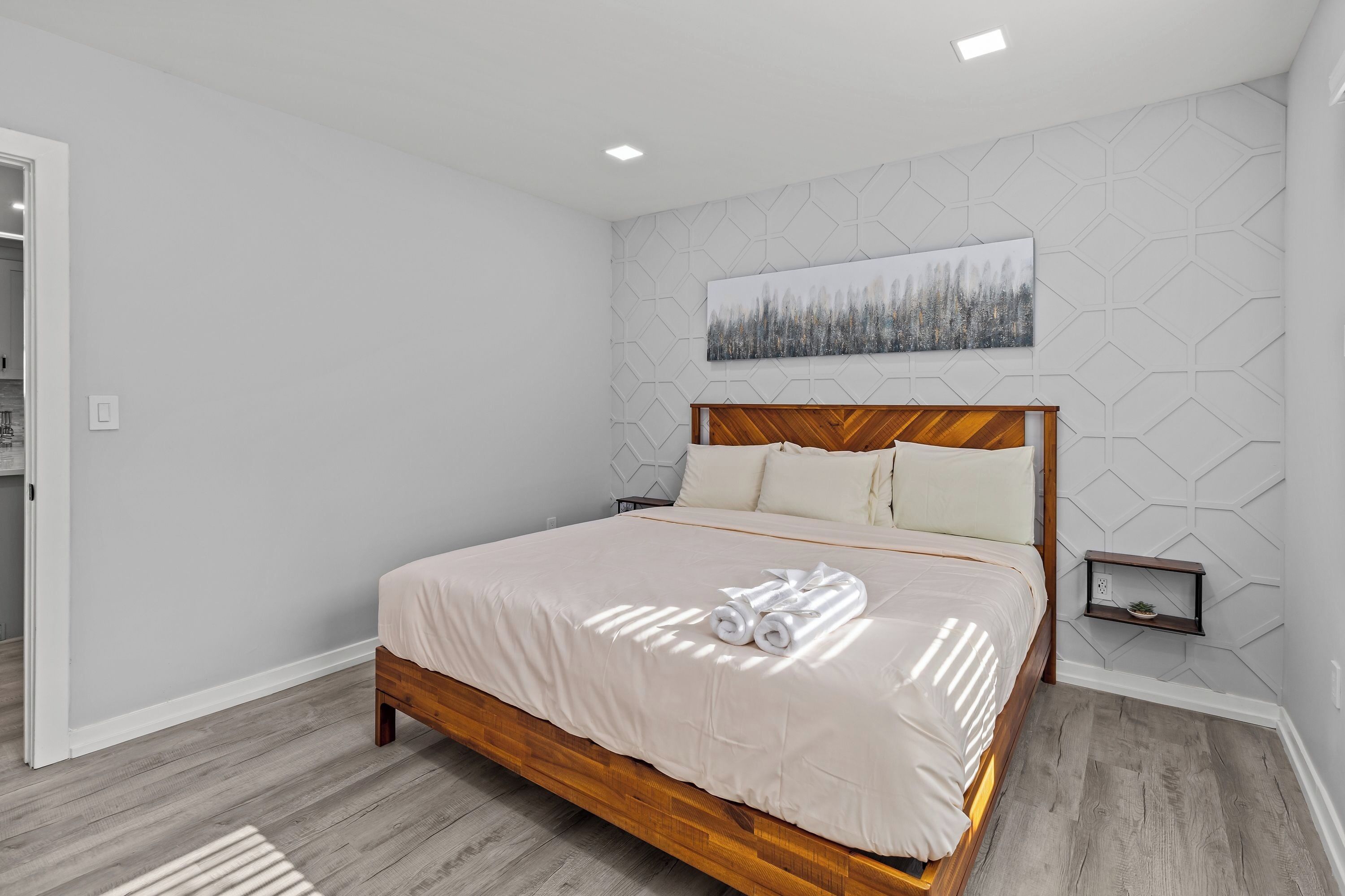 Een moderne slaapkamer met een houten bed, een wand met een geometrisch patroon en een schilderij erboven.