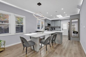 Une cuisine moderne avec un îlot central, des chaises recouvertes d’un tissu gris et une grande fenêtre.