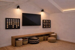 A room with a large flat-screen TV mounted on the wall, a wooden bench with storage baskets, and decorative wall art. - Hale Puka La, Luxury Oceanview for 8, Beach Access (Princeville)