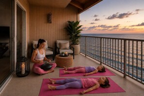 A balcony with a view of the sea, a woman meditating, and two children lying on yoga mats. - Hale Puka La, Luxury Oceanview for 8, Beach Access (Princeville)