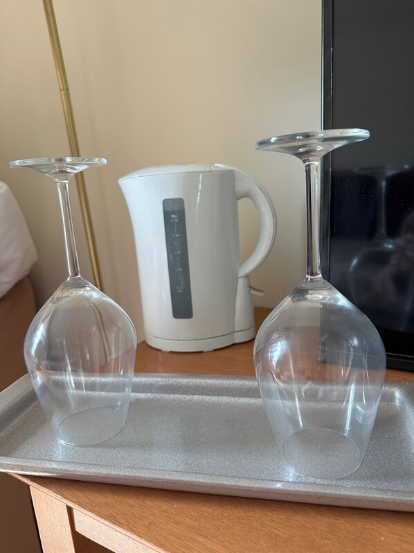A tray with two clear wine glasses and a white electric kettle on a wooden surface.