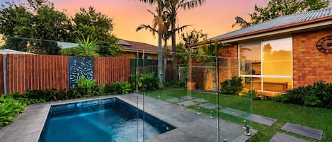 Un patio trasero con piscina, cerca de madera y una casa de ladrillo con ventanas amplias.